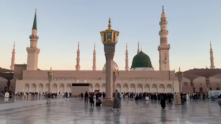 Pelgrims op het plein van de Moskee van de Profeet in Medina, met de groene koepel en de minaretten bij zonsondergang